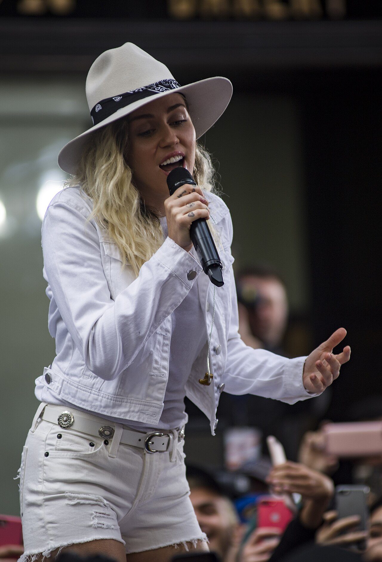 Miley Cyrus singing outdoors in a white hat and white denim jacket in 2017