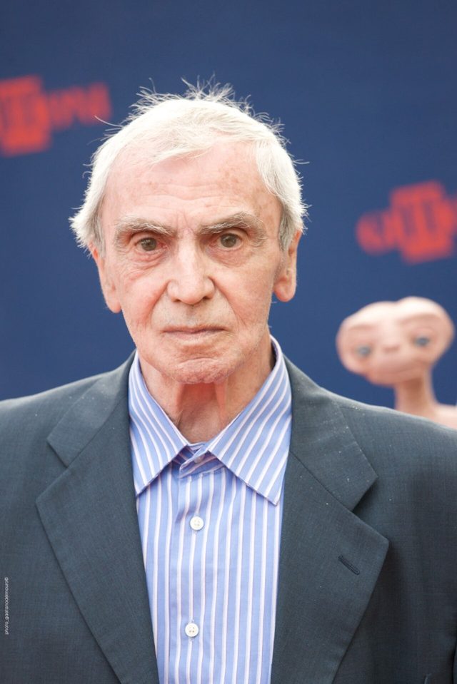 Carlo Rambaldi in a gray jacket against a blue backdrop with an E.T. figure behind him at the Giffoni Film Festival in 2010