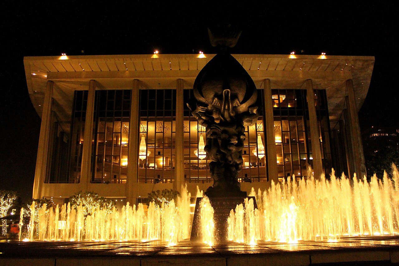 The Dorothy Chandler Pavilion lit at night behind the Music Center plaza fountains