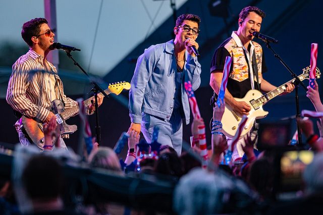 Nick, Joe and Kevin Jonas performing together onstage with guitars and microphones