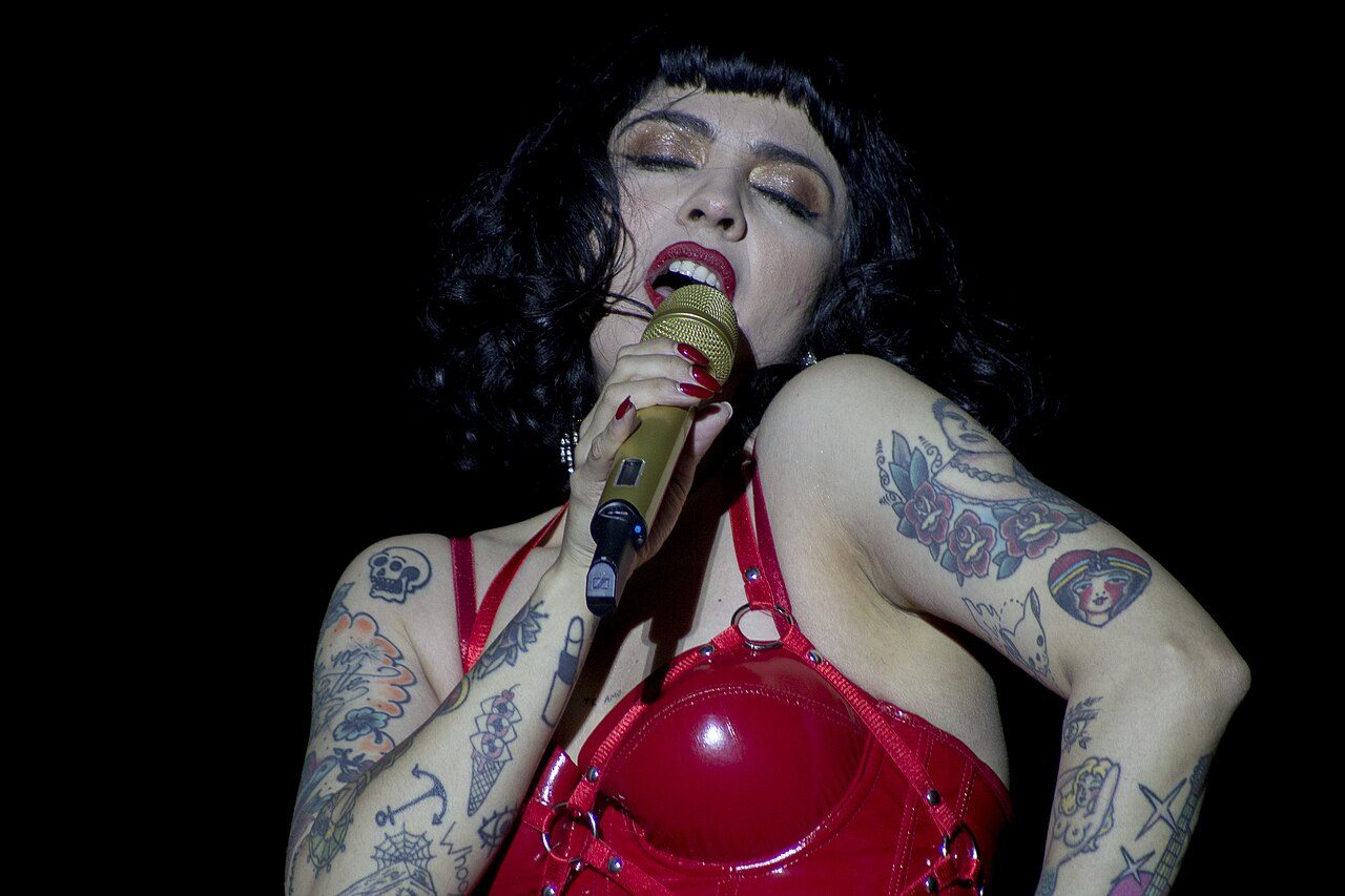 Mon Laferte singing into a microphone on stage in a red corset in 2020
