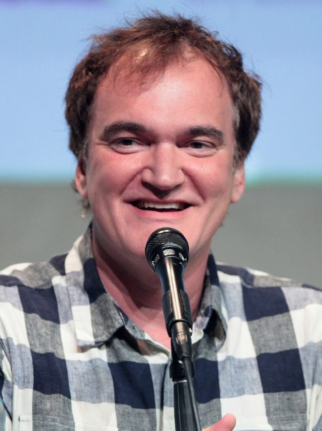 Quentin Tarantino smiling at a microphone during a 2015 Comic-Con panel