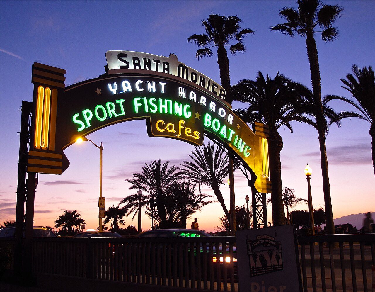 The neon Santa Monica Yacht Harbor sign at the pier entrance at dusk, framed by palm trees