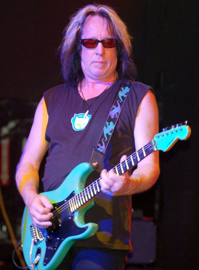 Todd Rundgren playing a teal electric guitar on stage in 2009