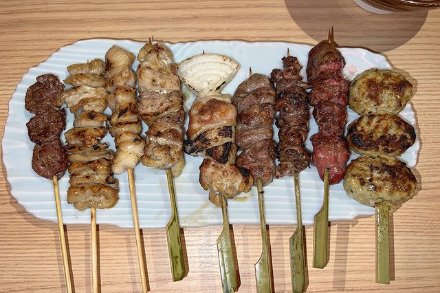 A row of charcoal-grilled yakitori skewers on a white plate