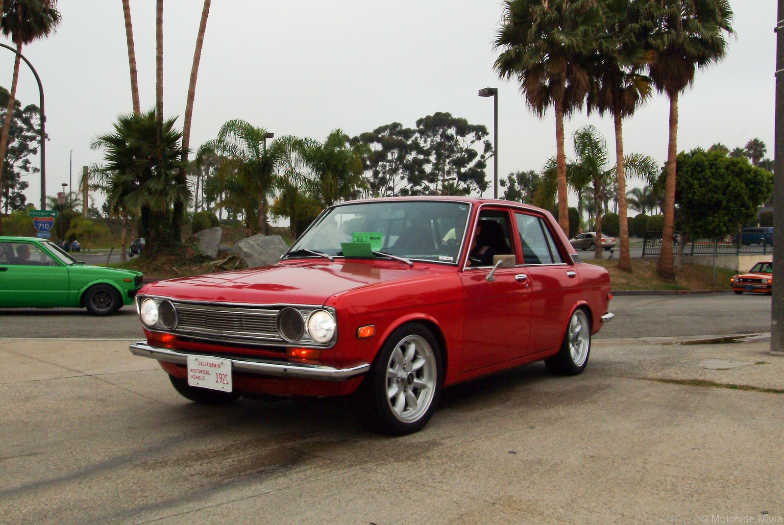A red Datsun 510 sedan on show with palm trees behind it
